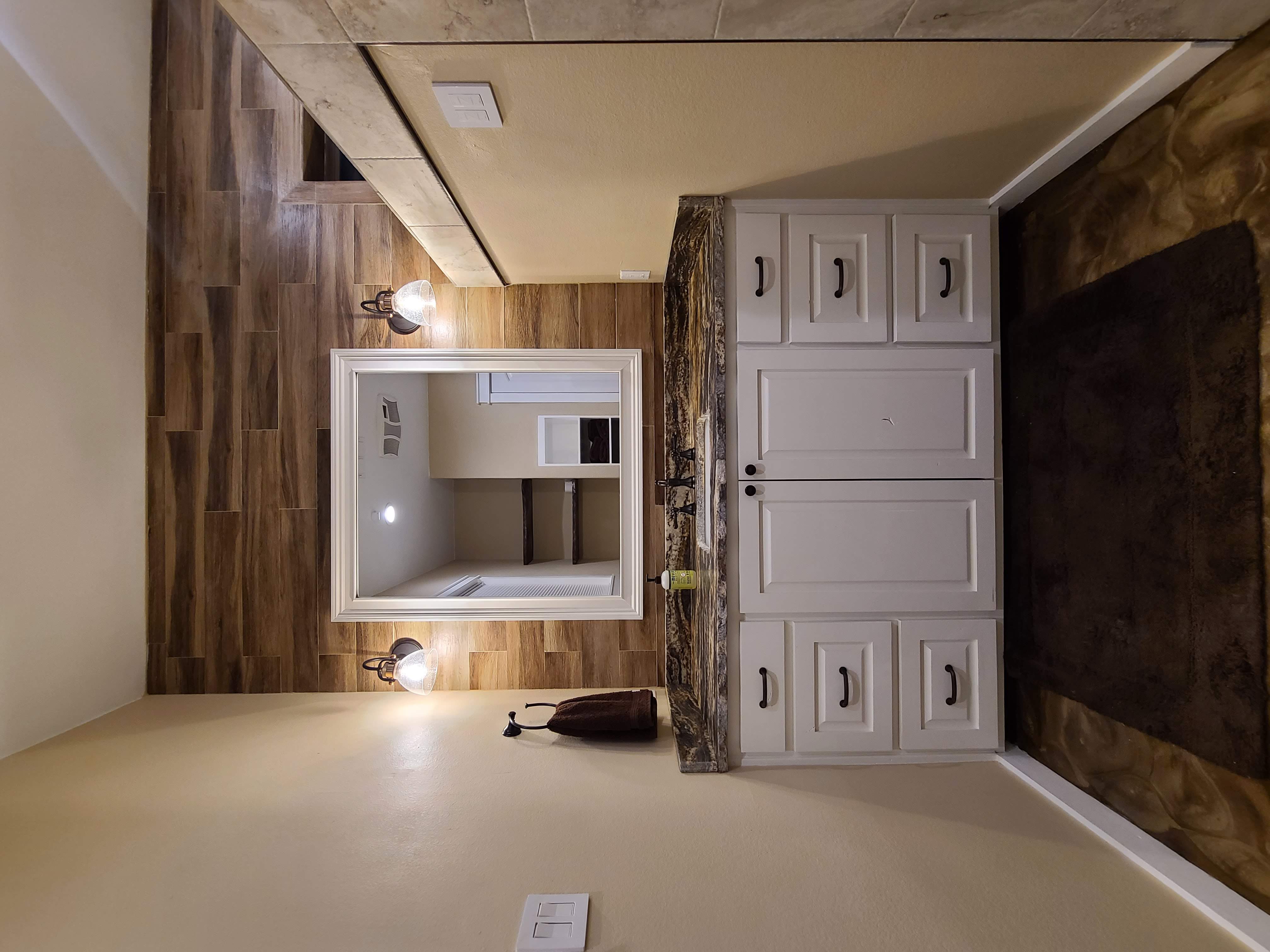 Bathroom white vanity wood tile accent wall granite countertop sconce lighting