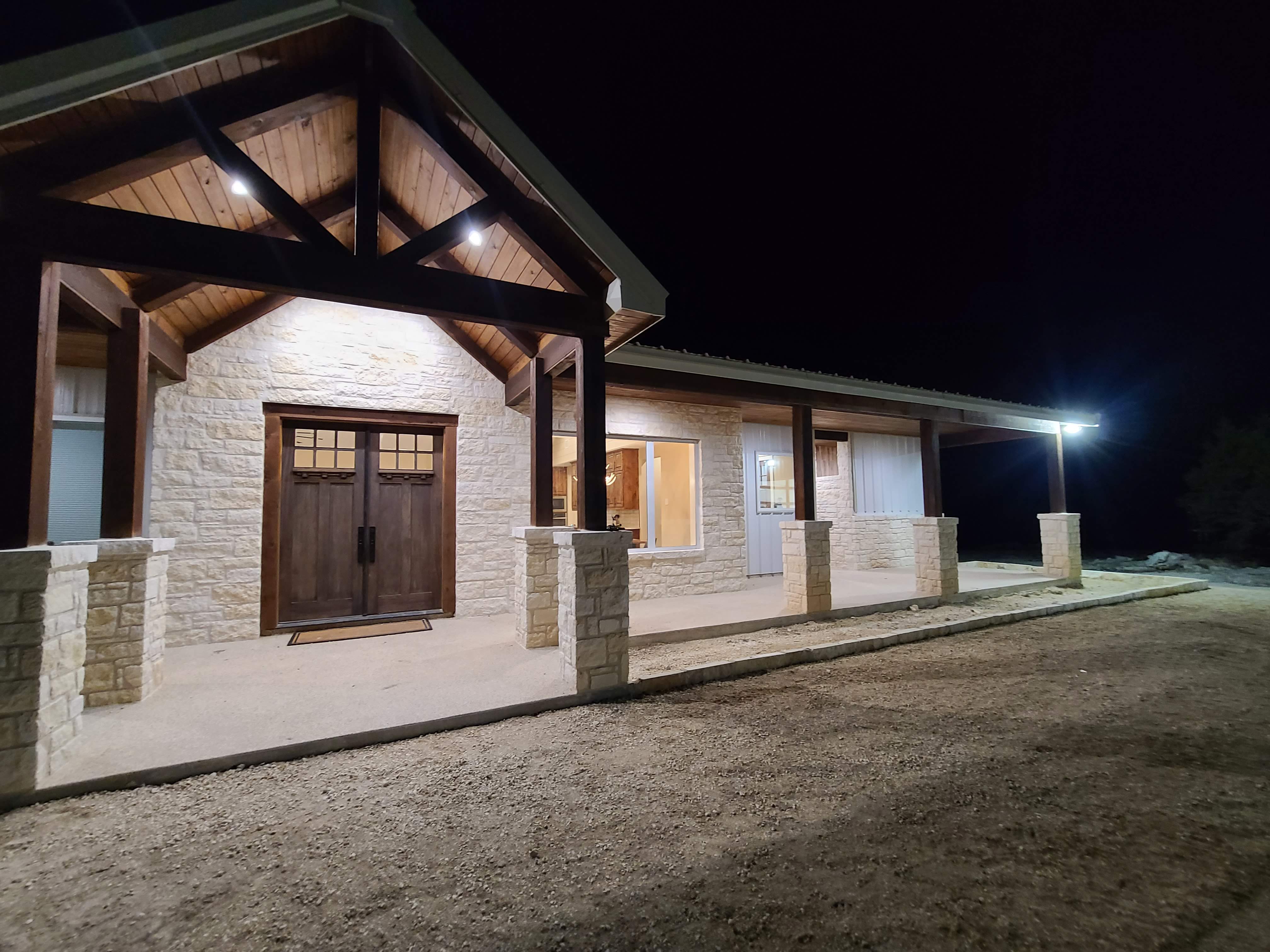 Custom Texas Hill Country ranch home — limestone exterior, timber frame entry, metal roof, night